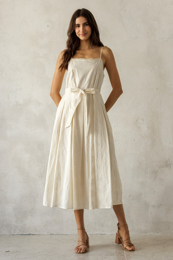 woman wearing a cream-colored midi dress with adjustable spaghetti straps and a waist tie detail