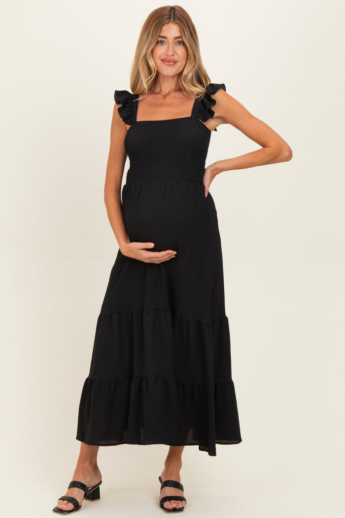woman wearing a black ruffle strap maternity maxi dress and holding her baby bump