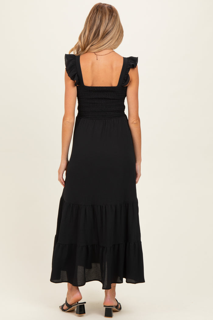 woman wearing a black sleeveless maternity dress with ruffle details and a tiered skirt, showing her baby bump from the back