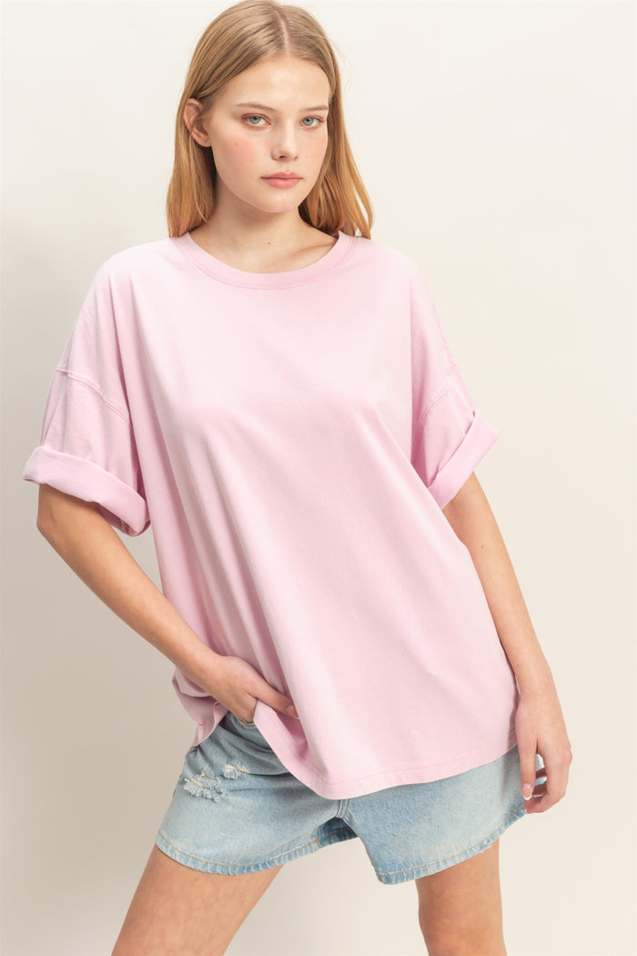 woman wearing a light pink oversized t-shirt with rolled sleeves and distressed denim shorts