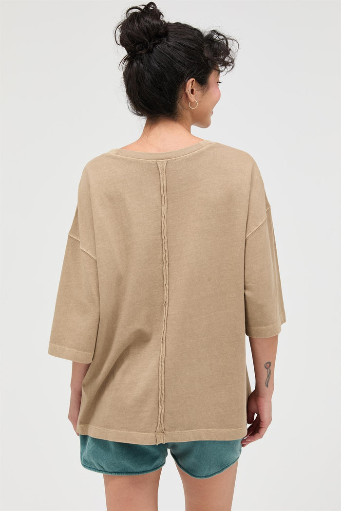 woman wearing a beige oversized t-shirt with a braided seam detail at the back, styled with teal shorts