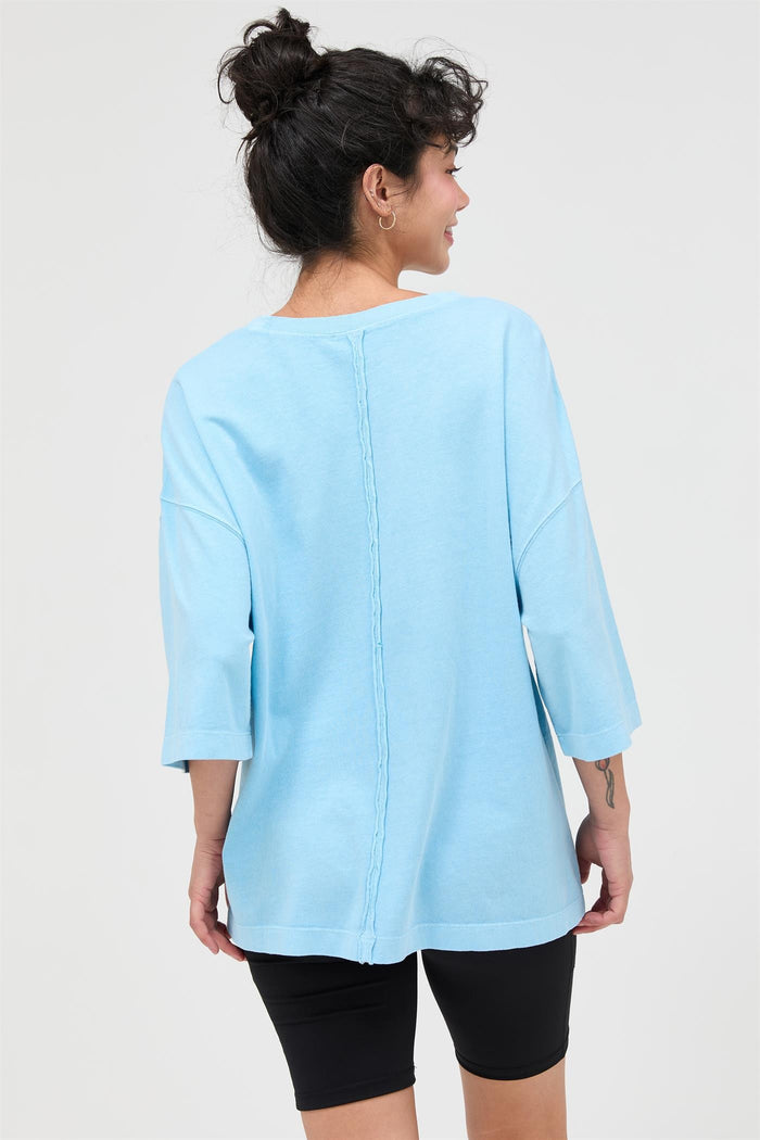 woman wearing a light blue oversized top with three-quarter sleeves and a textured back seam, paired with black bike shorts