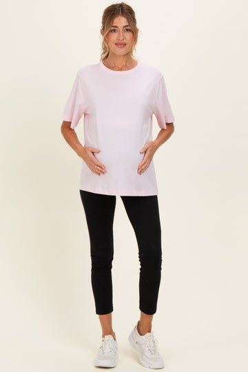 woman wearing a pink short sleeve maternity top and black leggings, holding her baby bump