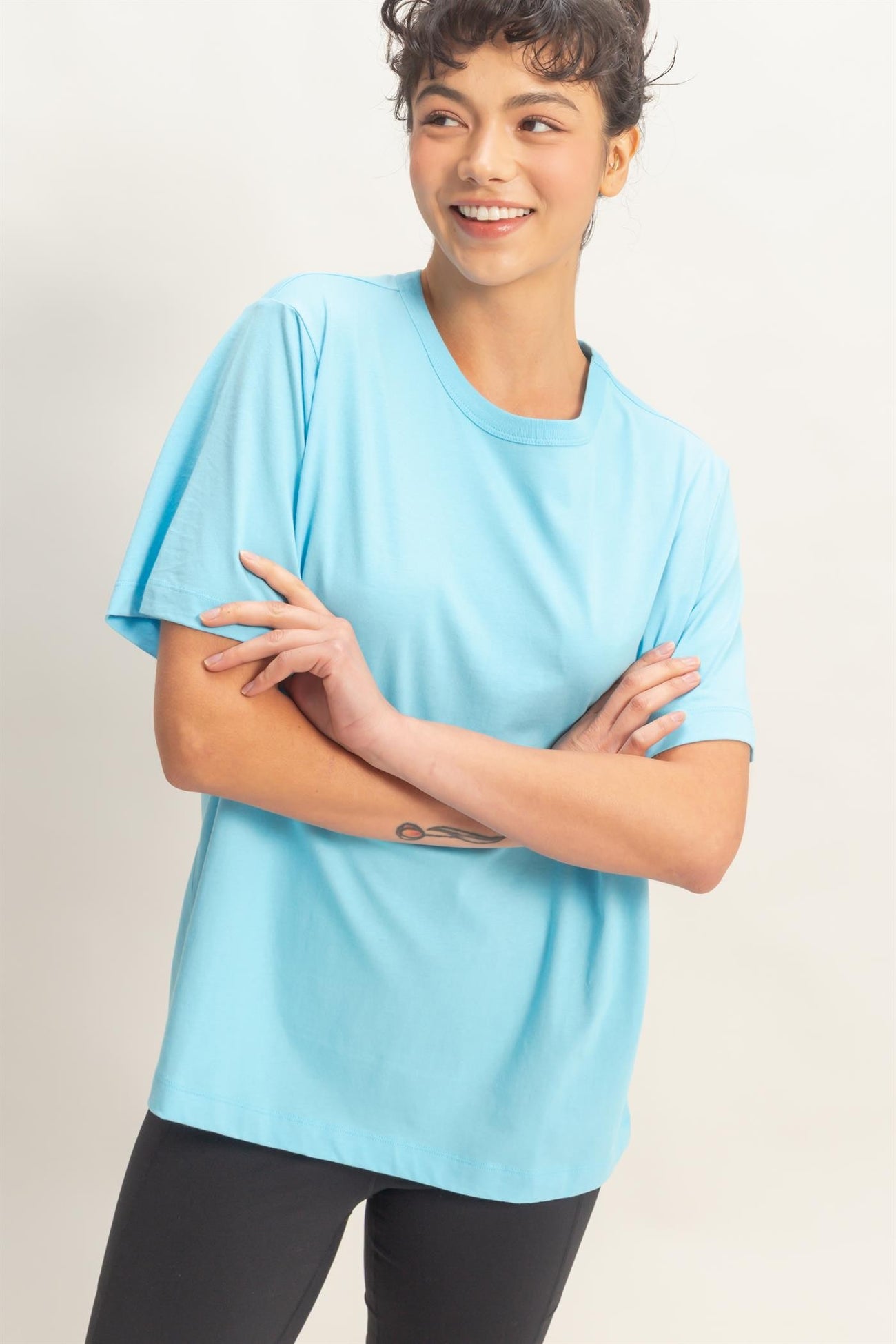 woman wearing a light blue short sleeve t-shirt and black leggings, smiling with arms crossed