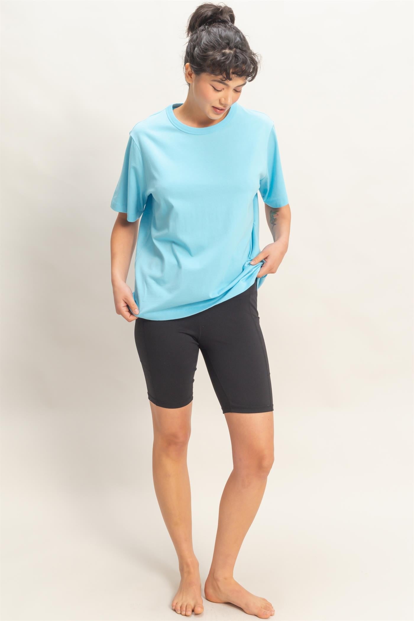 woman wearing a light blue short sleeve athletic top and black bike shorts, standing barefoot