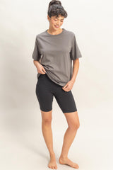 woman wearing a gray short sleeve t-shirt and black bike shorts, standing barefoot against a neutral background