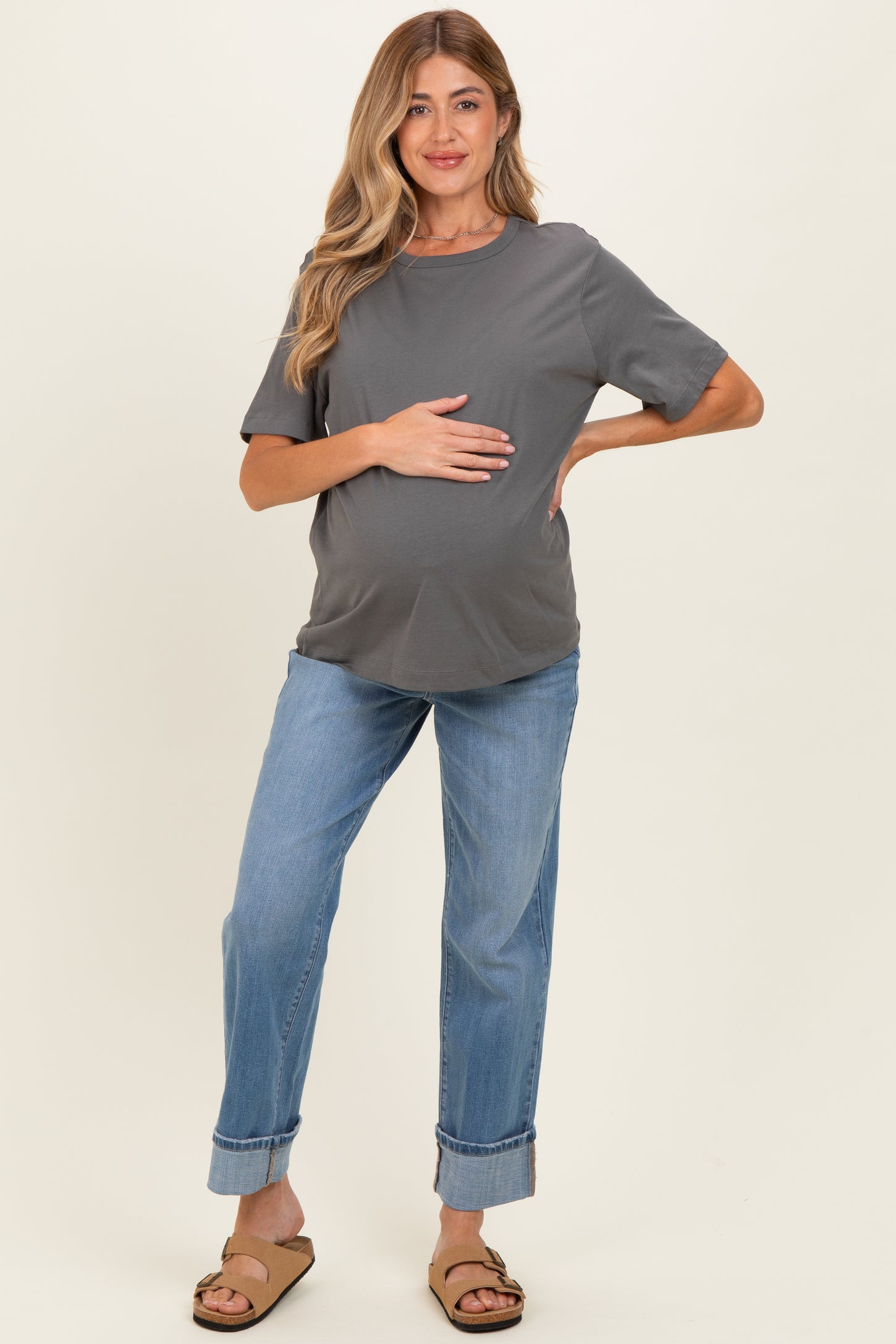 woman wearing a gray short sleeve maternity top and blue rolled hem jeans, holding her baby bump
