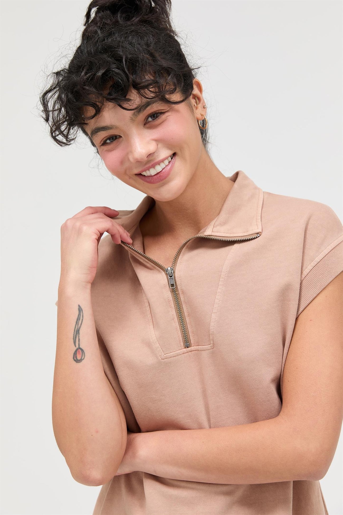 woman wearing a beige short sleeve zip-up polo top and smiling at the camera