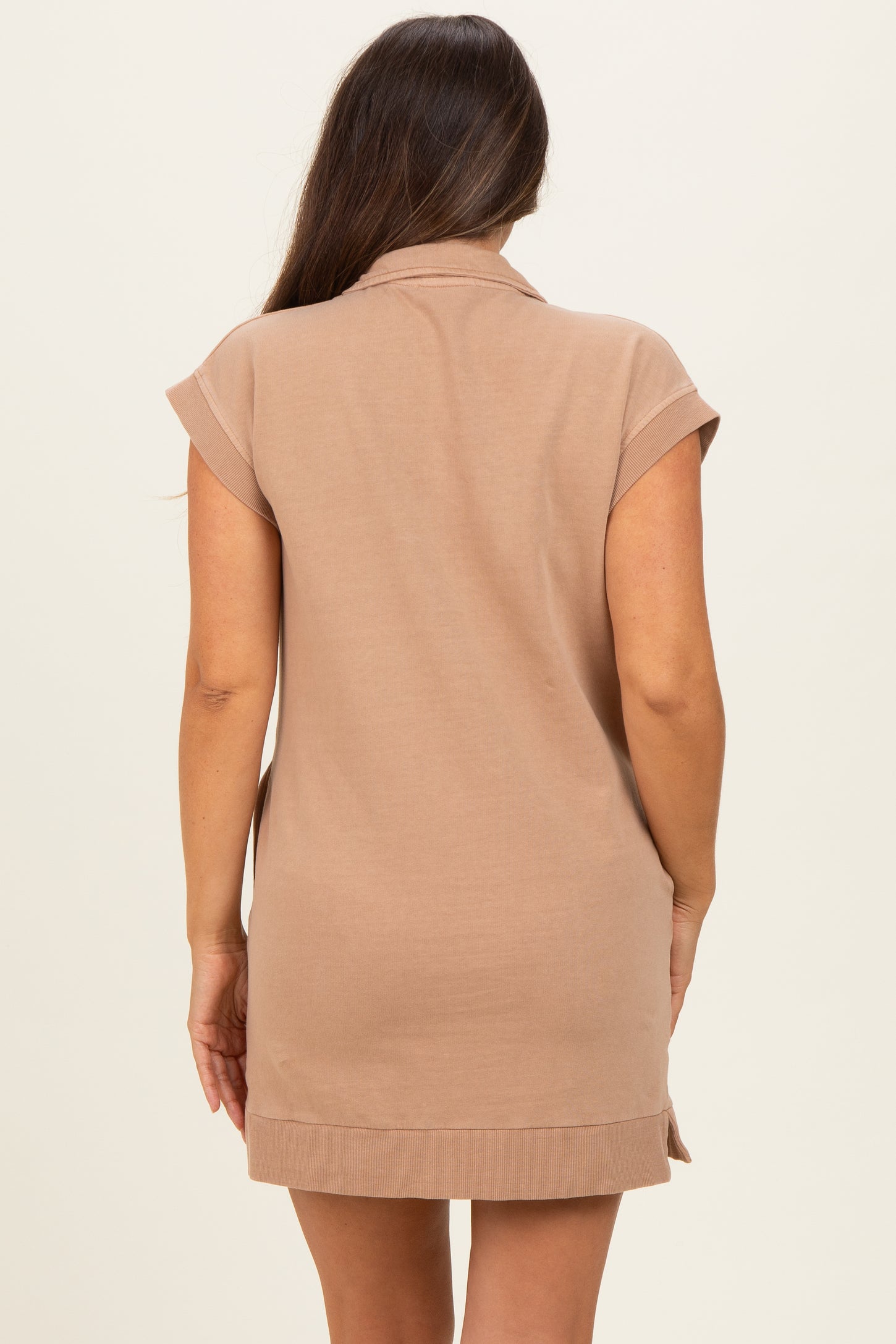 woman wearing a beige short sleeve maternity dress viewed from the back, styled with a collar and side slits