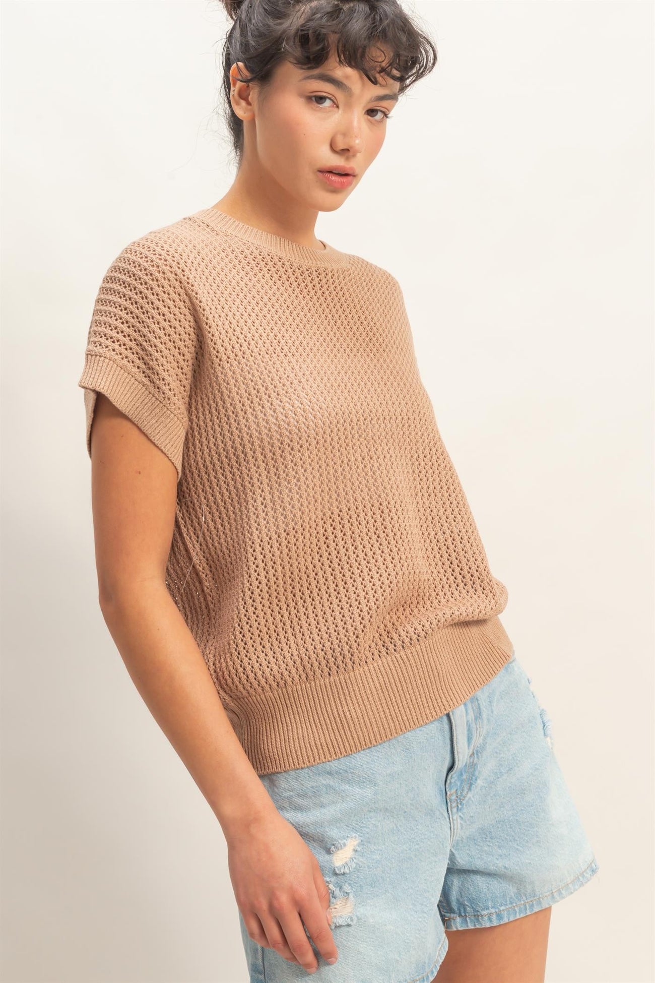 woman wearing a beige knit short sleeve sweater with a relaxed fit and paired with light blue distressed denim shorts