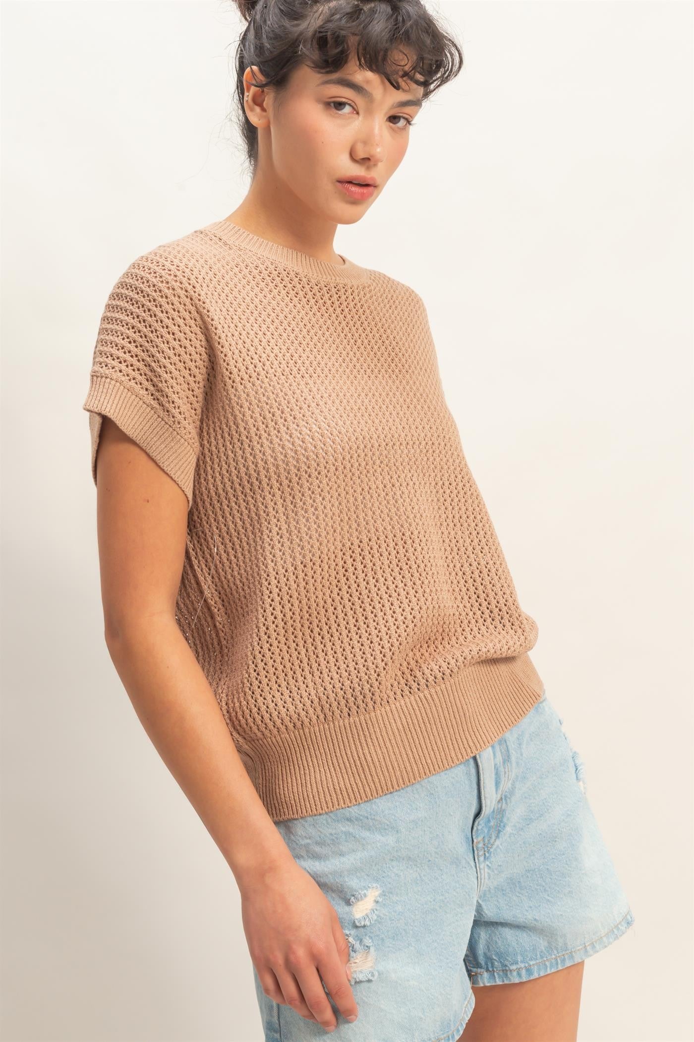 woman wearing a beige knit short sleeve sweater with a relaxed fit and paired with light blue distressed denim shorts