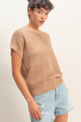 woman wearing a beige knit short sleeve sweater with a relaxed fit and paired with light blue distressed denim shorts