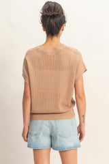 woman wearing a beige knit short sleeve sweater and light denim shorts, viewed from the back