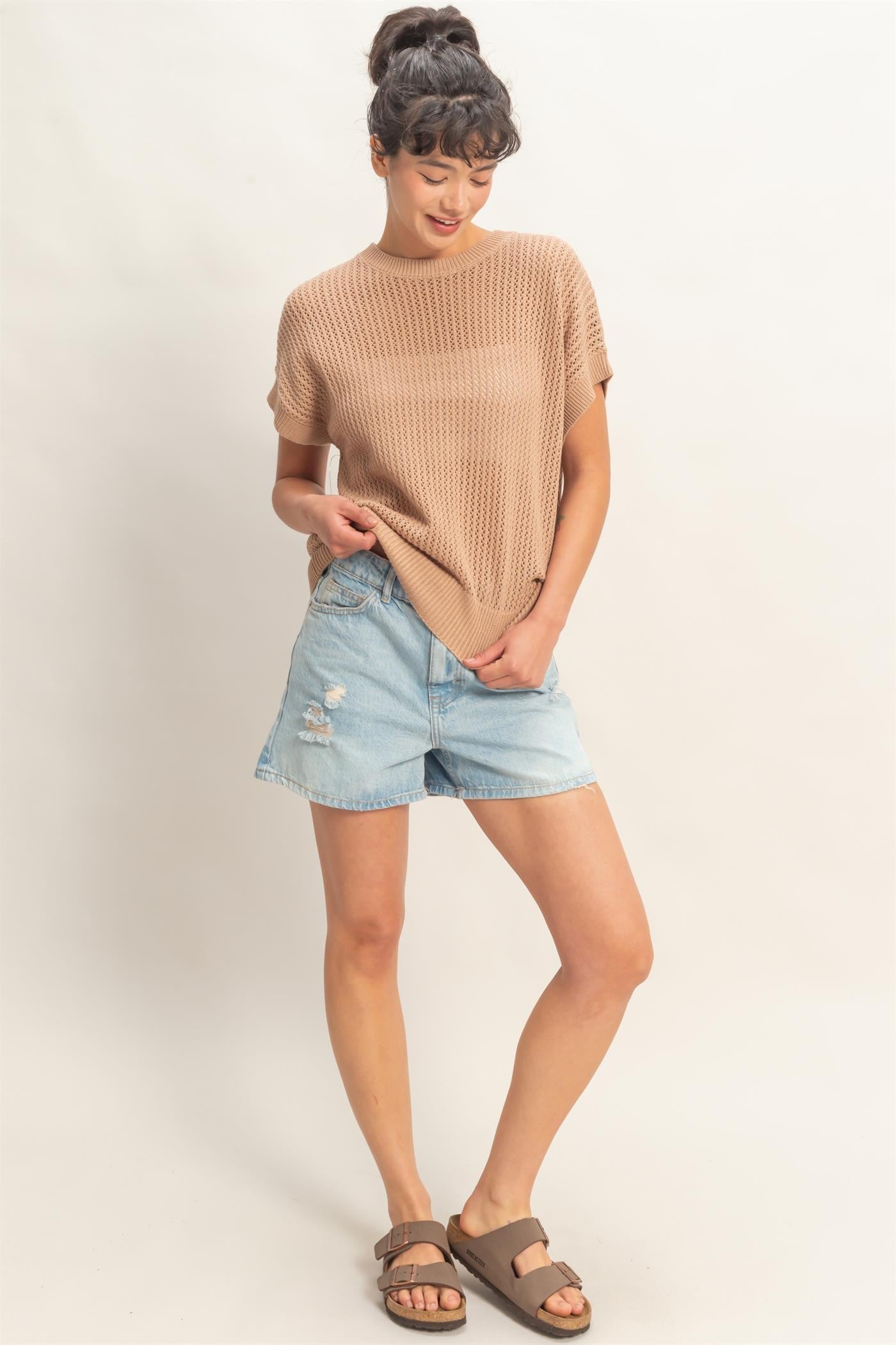 woman wearing a beige knitted short sleeve sweater and distressed denim shorts with brown sandals