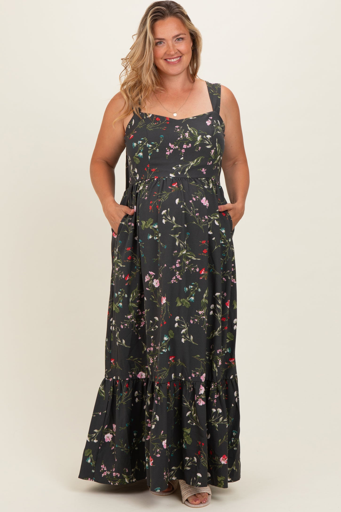 woman wearing a black floral maternity maxi dress with pockets and a tiered skirt