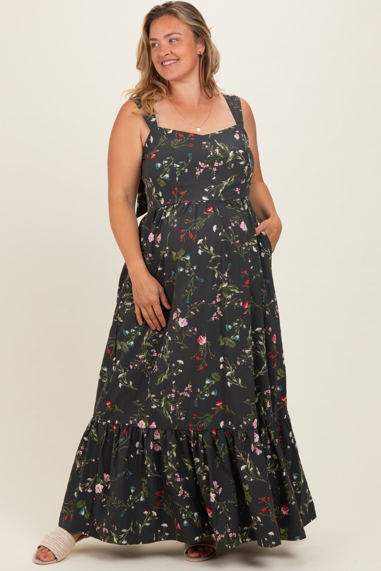 woman wearing a black floral print maternity plus maxi dress with a tiered skirt and pockets