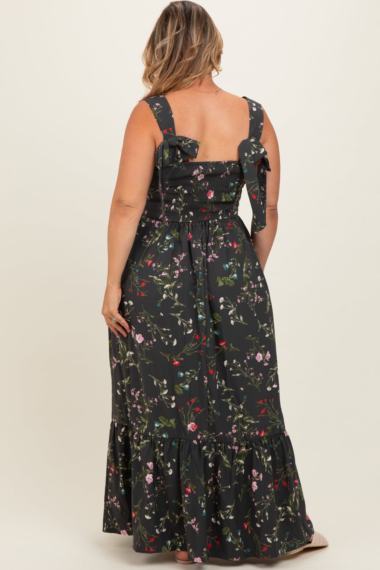 woman wearing a black floral print maternity plus maxi dress with smocked back and bow detail on shoulder straps