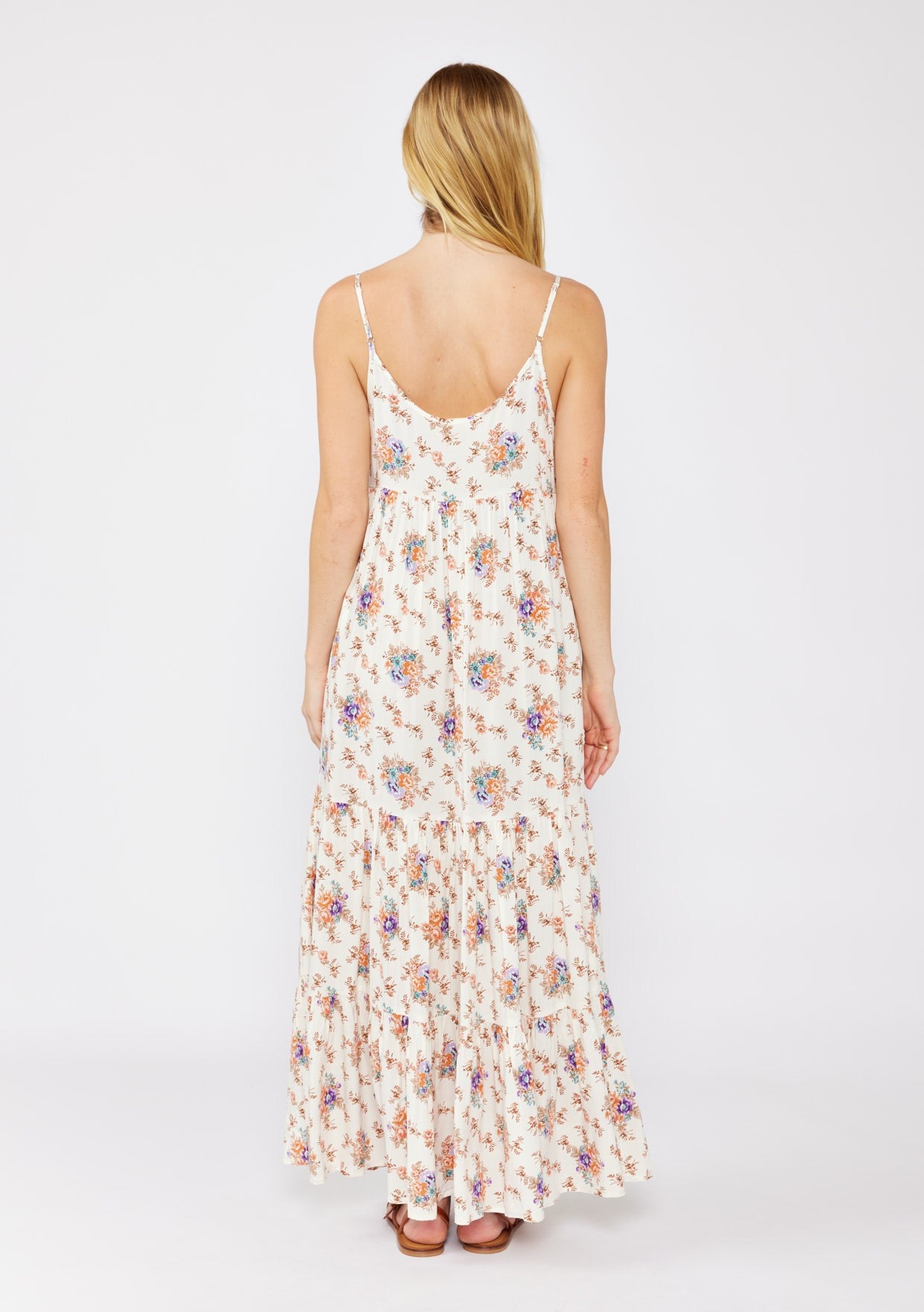 woman wearing a floral maxi dress with thin straps and a tiered hem, viewed from the back