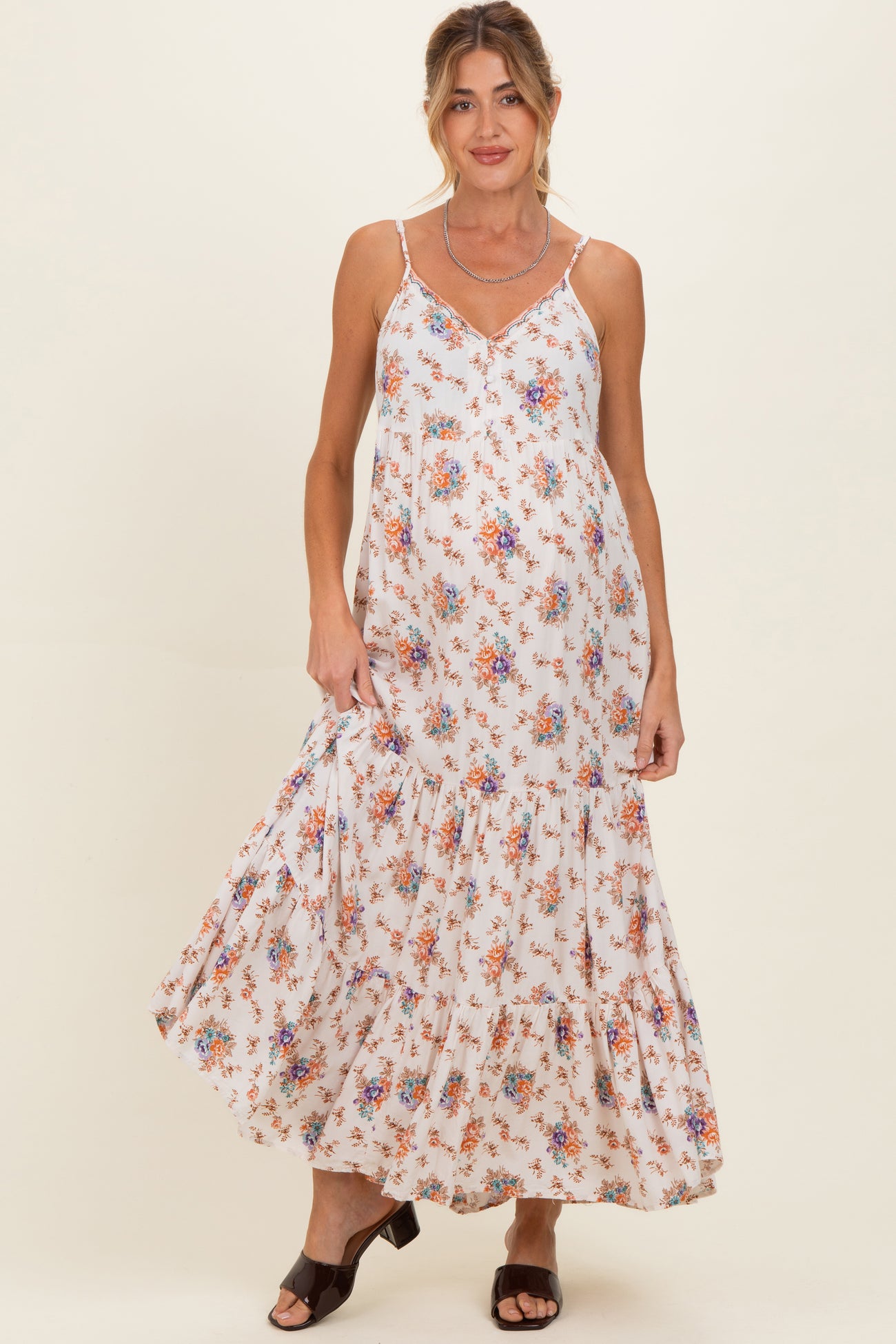woman wearing a white floral maternity maxi dress with a tiered skirt and adjustable straps, highlighting her baby bump