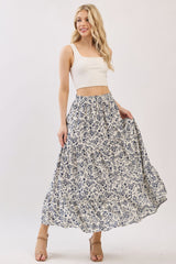 woman wearing a white crop top and a flowing blue floral print maxi skirt, smiling with hands in pockets