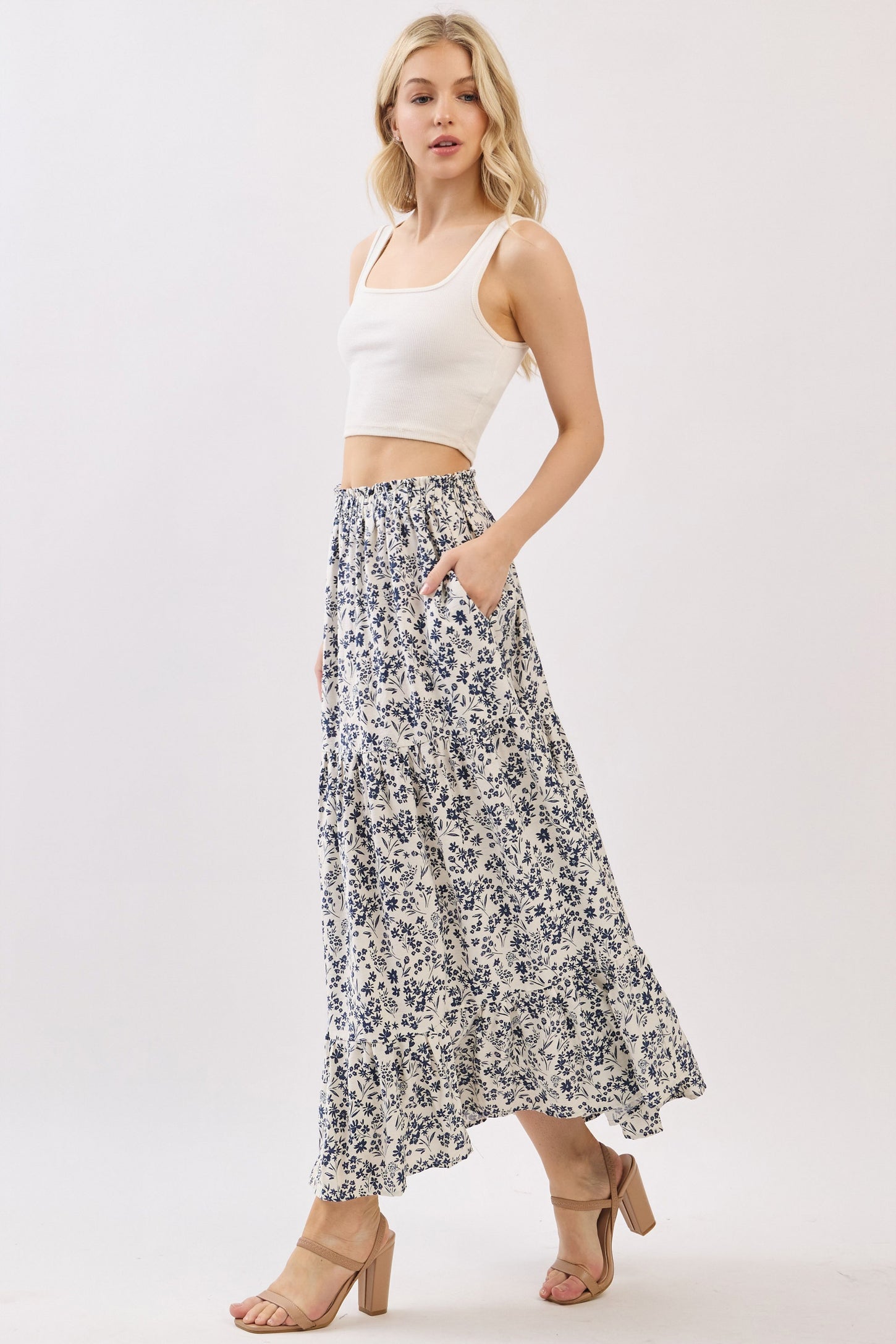 woman wearing a white crop top and a floral maxi skirt with pockets, standing on a light background