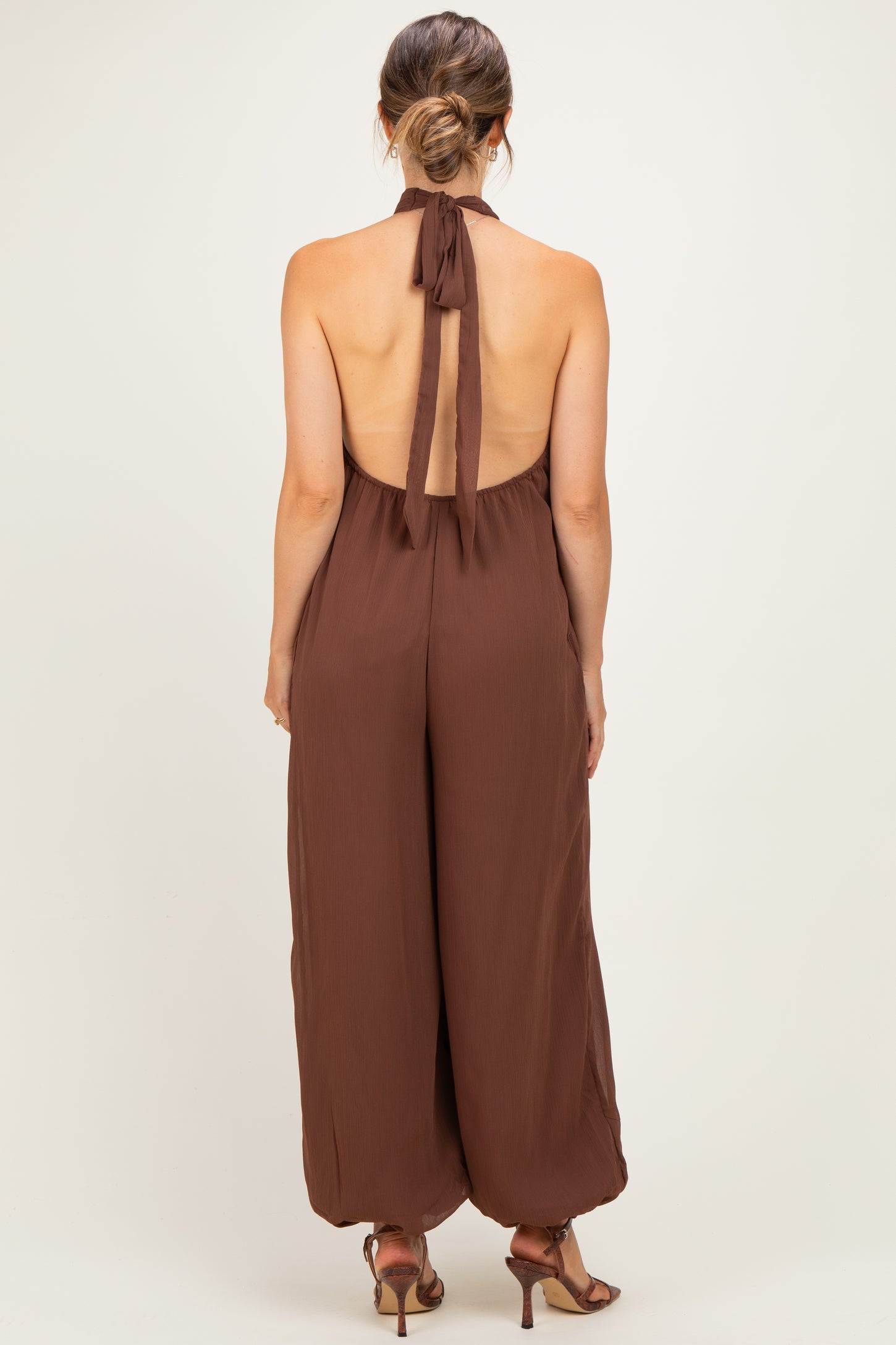 woman wearing a brown halter neck maternity jumpsuit with a flowing silhouette and an open back