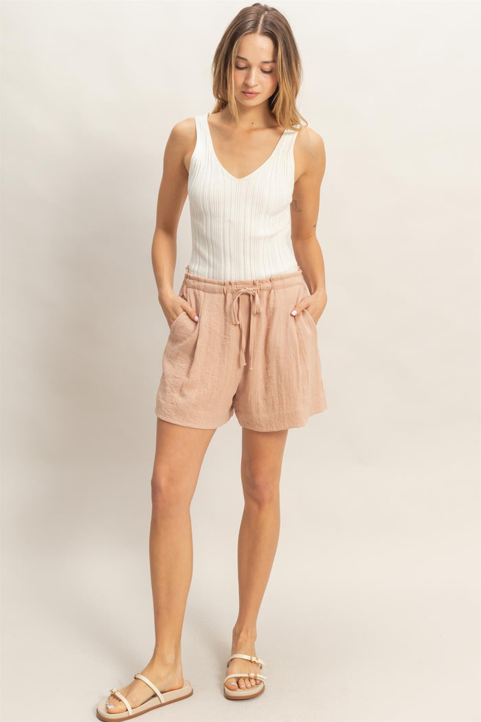 woman wearing a white sleeveless ribbed top and light pink drawstring linen shorts
