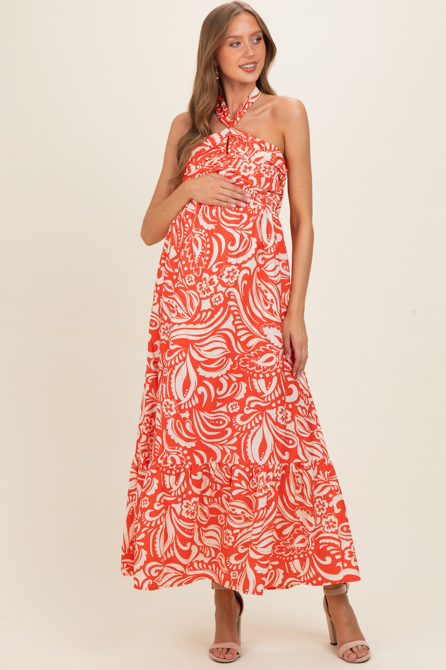woman wearing a red floral print maternity maxi dress with a halter neckline and holding her baby bump
