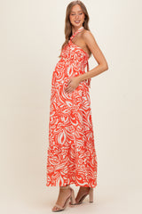 woman wearing a bright orange and white floral maternity maxi dress with a halter neckline and a visible baby bump