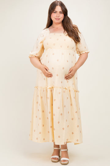 woman wearing a yellow floral maternity plus dress with short puff sleeves and a tiered skirt, cradling her baby bump