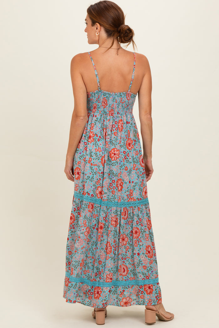 woman wearing a sleeveless maxi dress with a floral print in shades of blue, red, and green, showing a tiered design from the back