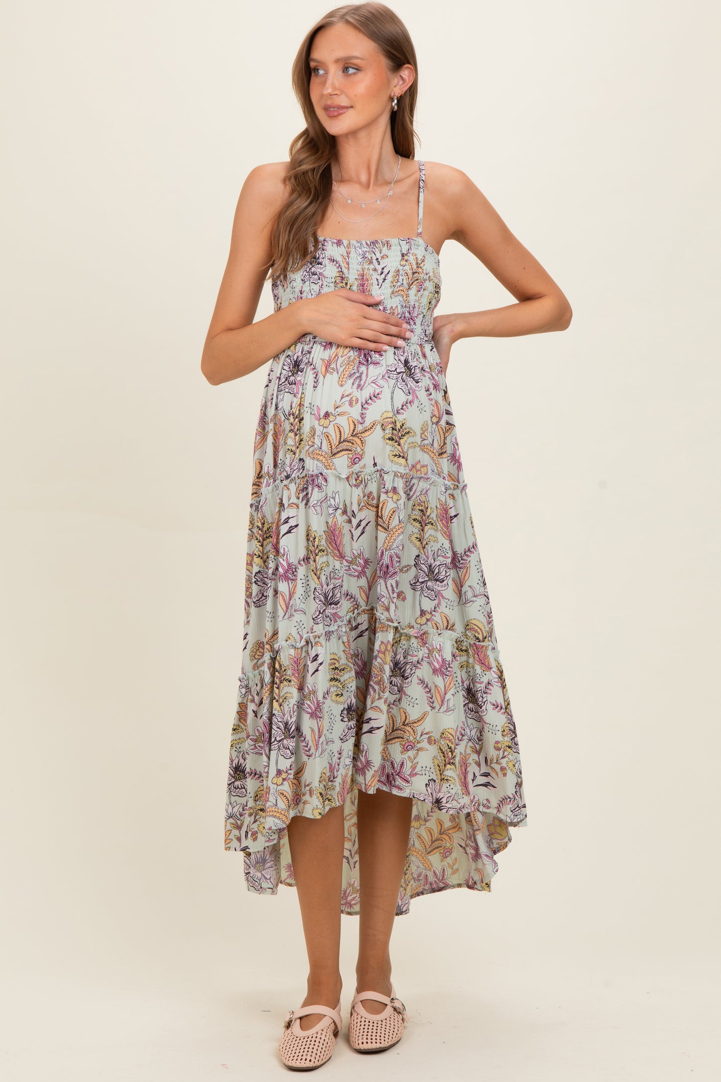 woman wearing a floral print maternity maxi dress, gently cradling her baby bump