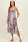 woman wearing a floral print maternity dress with adjustable straps and pockets, featuring a gathered bodice and mid-length skirt