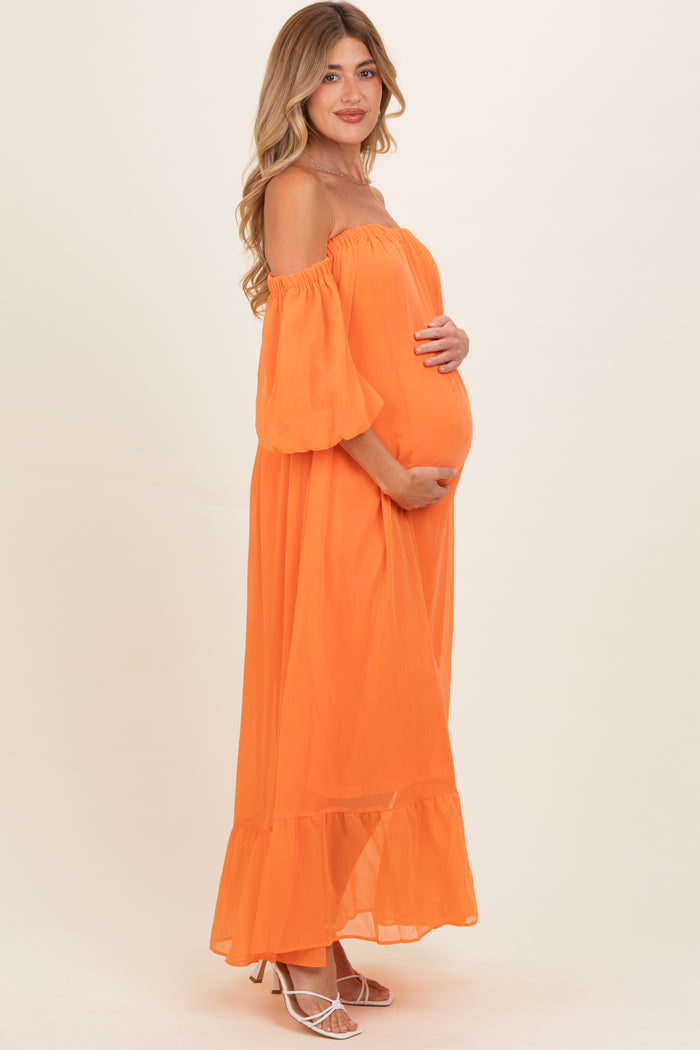 woman wearing an orange off-the-shoulder maternity dress and holding her baby bump