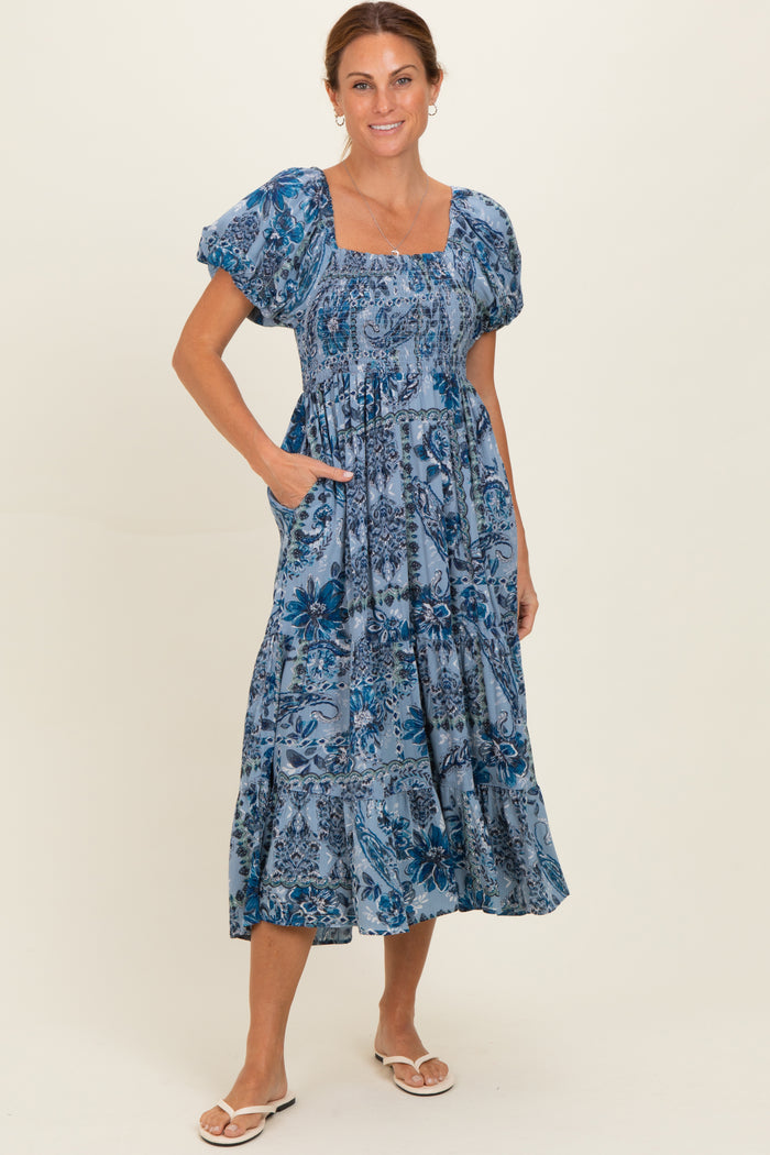 woman wearing a blue floral print midi dress with puff sleeves and pockets, standing on a light background