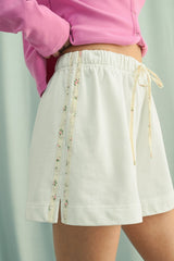 woman wearing white drawstring shorts with floral side detailing and a pink cardigan