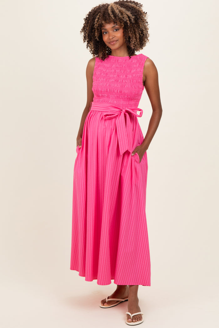woman wearing a bright pink maternity maxi dress with smocked bodice and bow detail at the waist, showing her baby bump