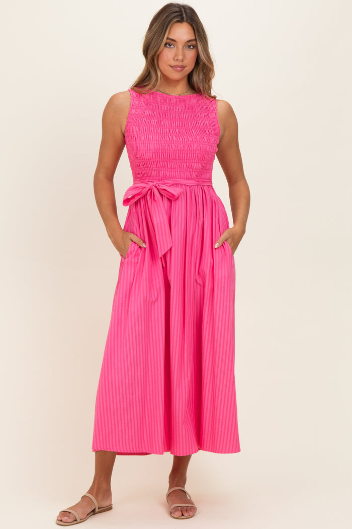 woman wearing a hot pink sleeveless dress with a smocked bodice and a tie waist, featuring side pockets