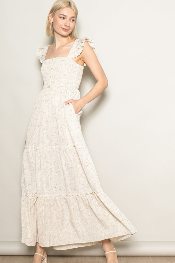 woman wearing a cream floral maxi dress with ruffled straps and pockets, standing against a neutral background
