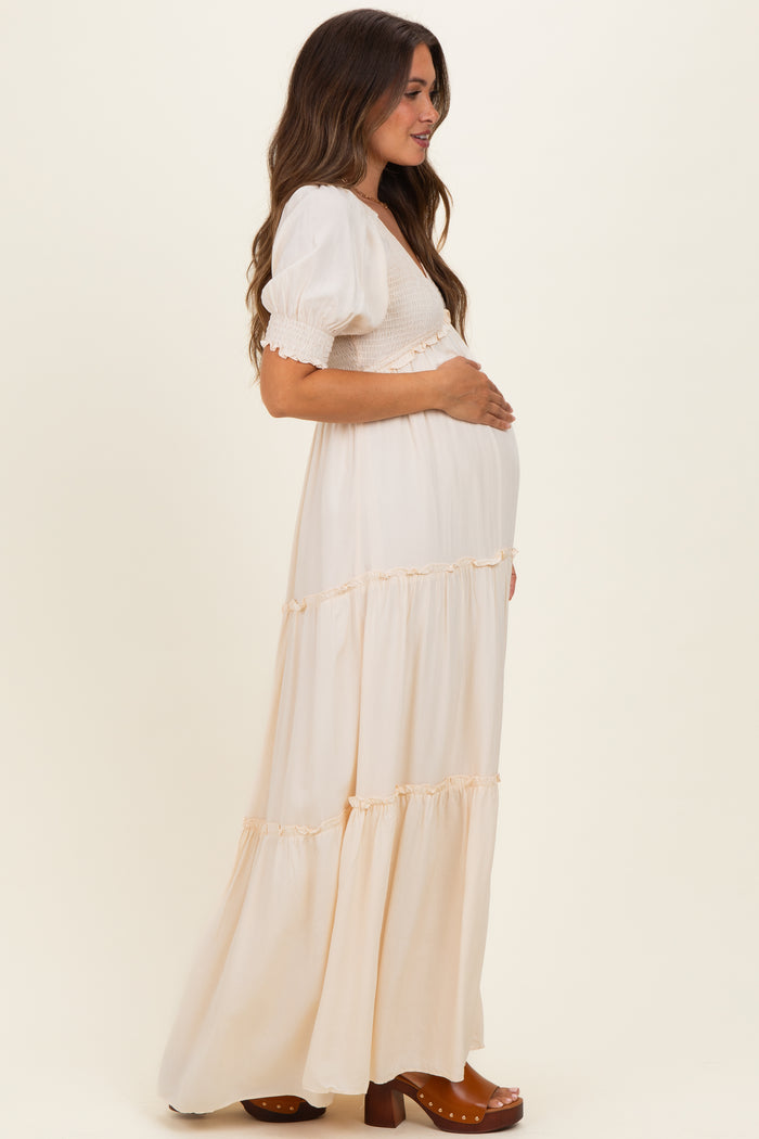 woman wearing a cream maternity maxi dress with puff sleeves and tiered ruffles, gently holding her baby bump
