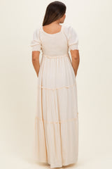 woman wearing a cream-colored maternity maxi dress with short puff sleeves and tiered skirt, showing a baby bump from the back