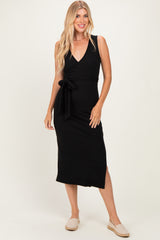 woman wearing a black sleeveless wrap dress with a tie at the waist and side slits, smiling at the camera