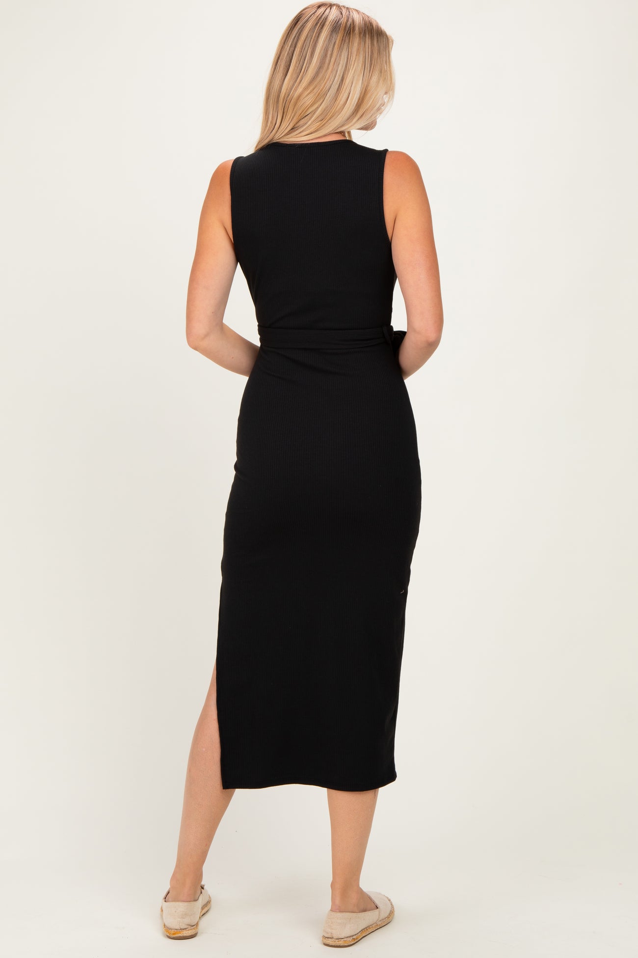 woman wearing a black sleeveless ribbed midi dress with a side slit, seen from the back