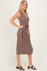 woman wearing a taupe sleeveless wrap dress with a tie waist and a midi length, styled with black sandals