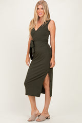 woman wearing an olive green sleeveless wrap dress with a tie and side slit, standing against a light background