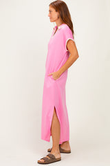 woman wearing a pink maxi dress with a collar and side slits, standing sideways with hands in pockets