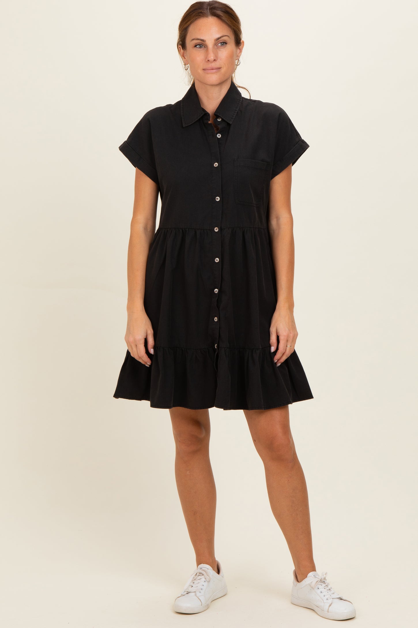 woman wearing a black short sleeve button-up dress with a tiered skirt and side pockets, styled with white sneakers