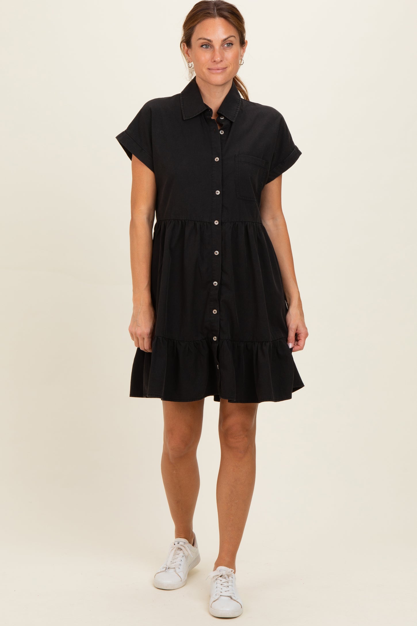 woman wearing a black button-up shirt dress with short sleeves and a ruffled hem, styled with white sneakers