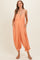 woman wearing a coral maternity jumpsuit with a button detail and pockets, featuring a loose fit and elastic cuffs