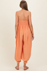 woman wearing a back view of a coral orange maternity jumpsuit with smocked bodice and loose-fitting pants